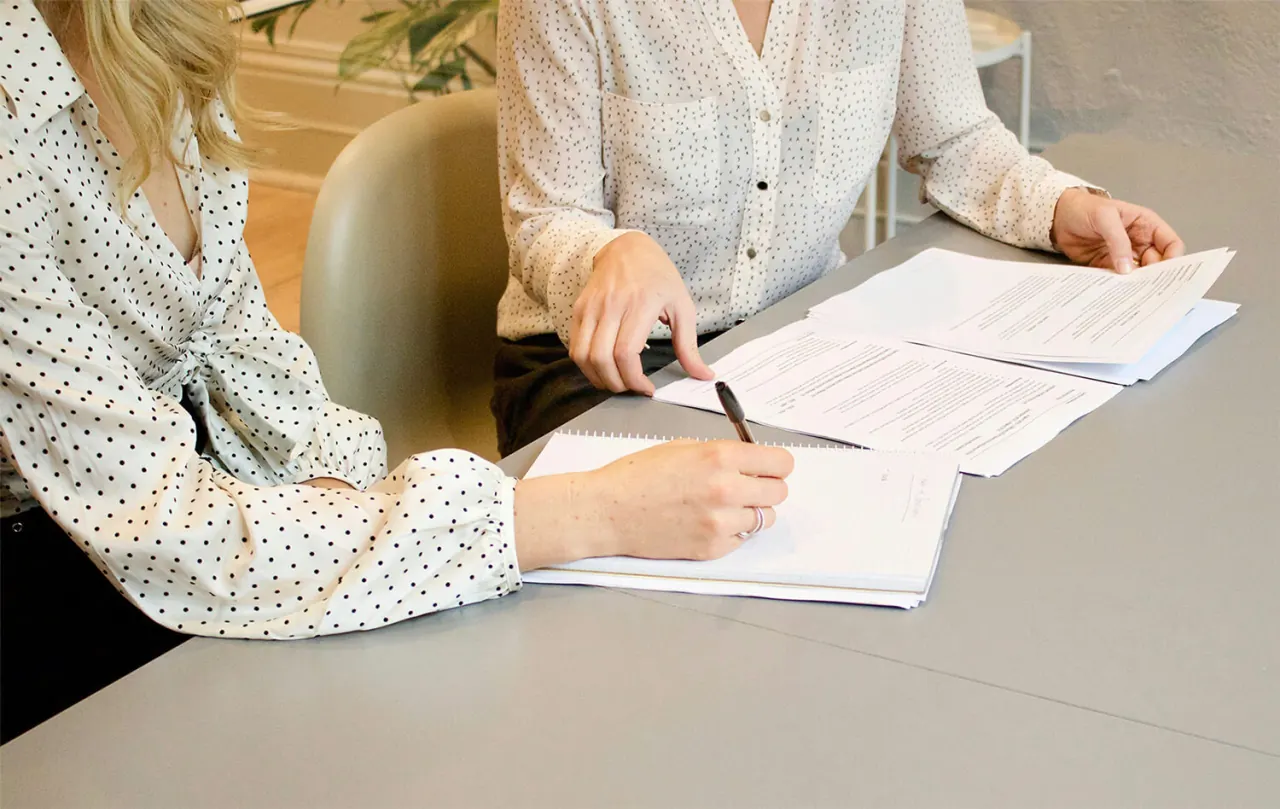 Zwei Personen am Schreibtisch, eine unterschreibt ein Schreiben